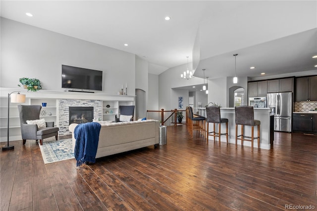 living room with vaulted ceiling, dark wood-type flooring, a stone fireplace, a chandelier, and recessed lighting