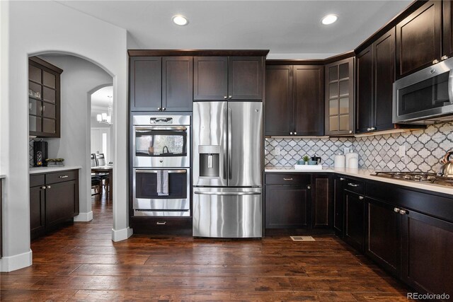 kitchen featuring stainless steel appliances, glass insert cabinets, dark wood-type flooring, light countertops, and tasteful backsplash