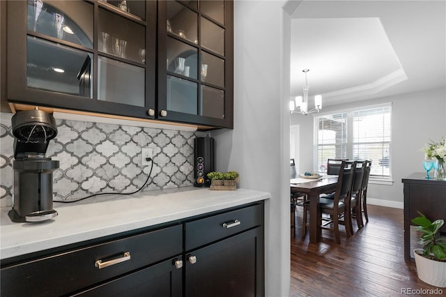 bar featuring an inviting chandelier, dark wood finished floors, baseboards, a raised ceiling, and backsplash