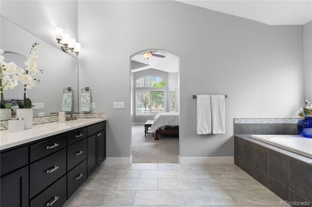ensuite bathroom with ensuite bathroom, vanity, a relaxing tiled tub, a ceiling fan, and baseboards
