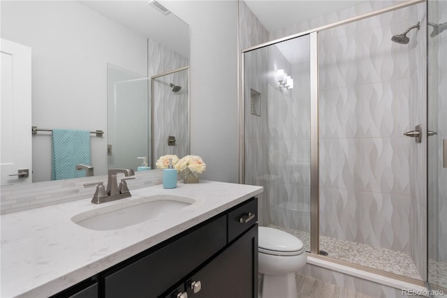 bathroom with a shower stall, toilet, vanity, and visible vents