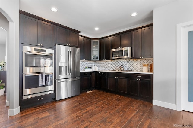 kitchen featuring glass insert cabinets, dark wood finished floors, arched walkways, light countertops, and appliances with stainless steel finishes