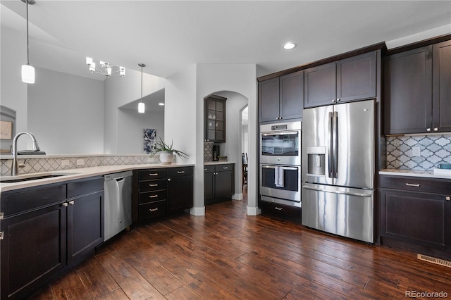 kitchen with a sink, tasteful backsplash, dark wood-style flooring, arched walkways, and appliances with stainless steel finishes