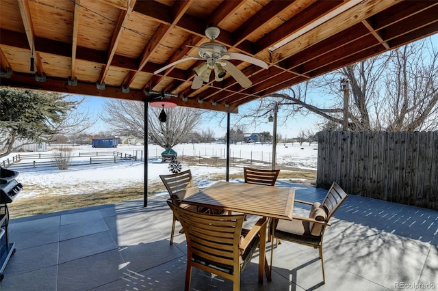 snow covered patio featuring ceiling fan, fence, and outdoor dining space