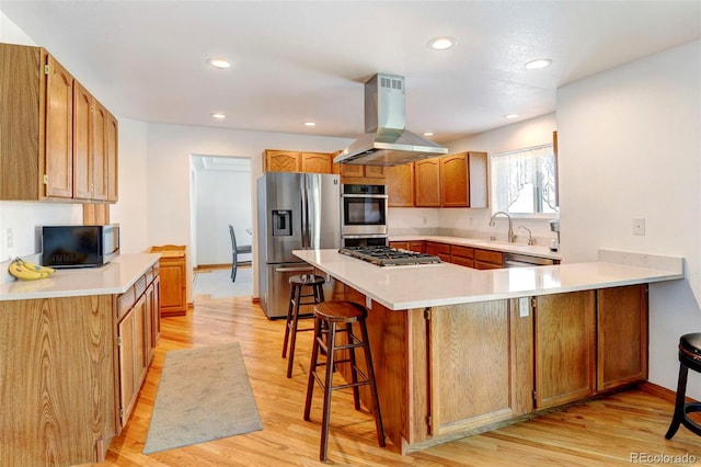 kitchen with a breakfast bar area, a peninsula, light countertops, appliances with stainless steel finishes, and island exhaust hood