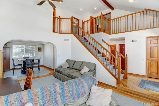 living area with arched walkways, beam ceiling, visible vents, high vaulted ceiling, and baseboards