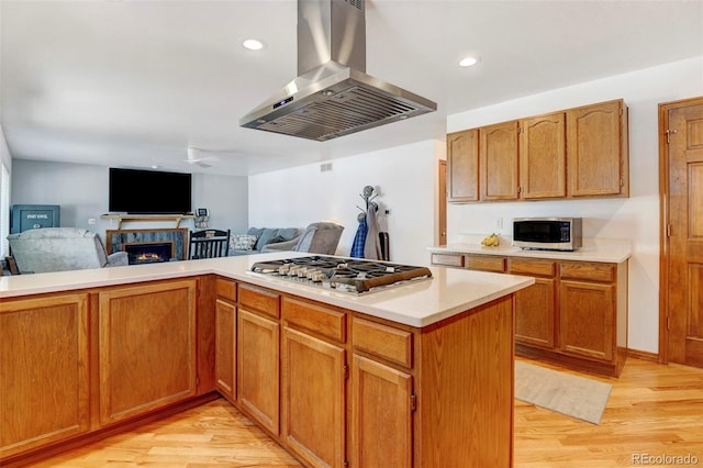 kitchen with appliances with stainless steel finishes, island range hood, open floor plan, and light countertops