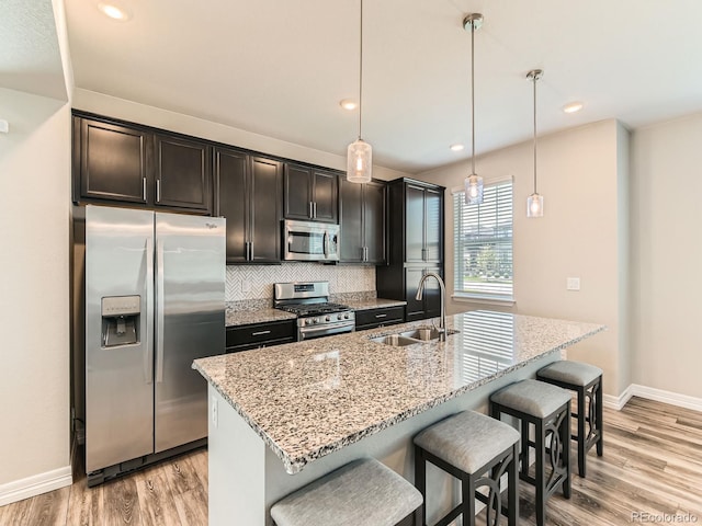 11902 Norfolk Ct, Commerce City, CO 80022 - kitchen featuring stainless steel appliances, decorative backsplash, light wood-style floors, a breakfast bar, and an island with sink