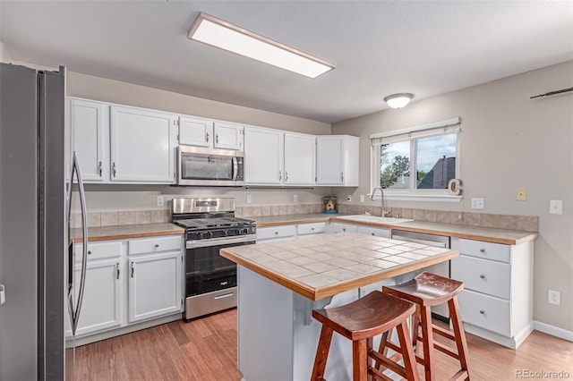 kitchen with appliances with stainless steel finishes, a sink, a breakfast bar, light wood finished floors, and white cabinetry