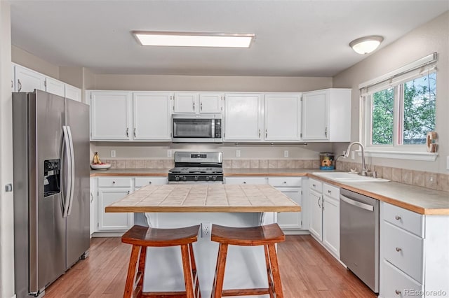 kitchen featuring stainless steel appliances, a sink, light wood-style flooring, a breakfast bar area, and white cabinets