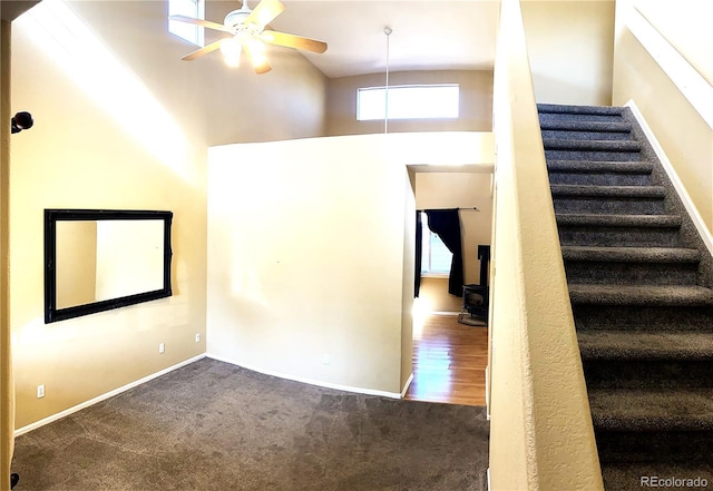interior space featuring a ceiling fan, a wood stove, baseboards, a high ceiling, and carpet flooring