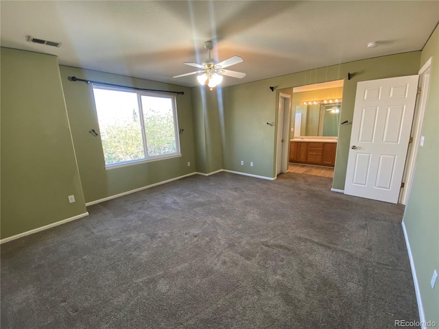 unfurnished bedroom with ensuite bath, dark carpet, a ceiling fan, baseboards, and visible vents
