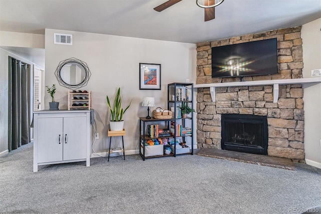 carpeted living room with a stone fireplace and ceiling fan