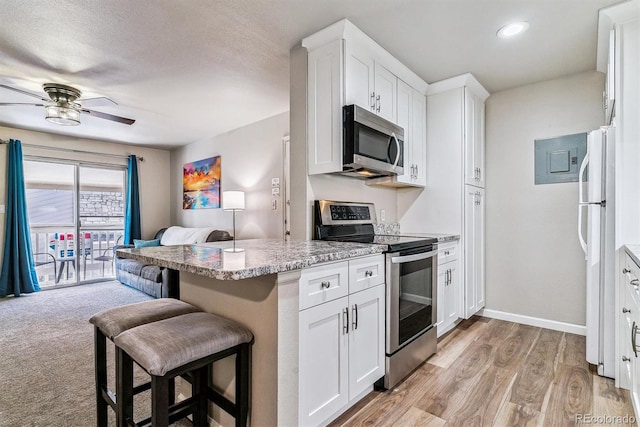 kitchen featuring ceiling fan, appliances with stainless steel finishes, white cabinetry, light stone countertops, and a kitchen bar