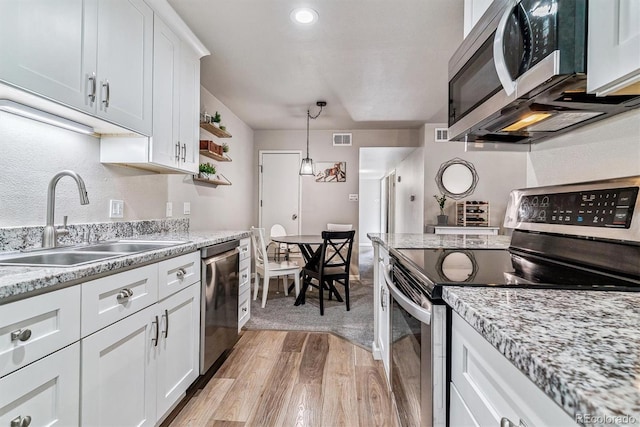 kitchen with sink, appliances with stainless steel finishes, white cabinets, decorative light fixtures, and light wood-type flooring