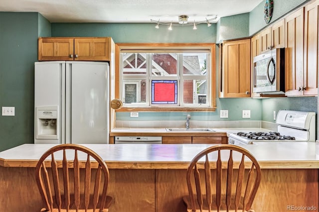 kitchen with a textured ceiling, kitchen peninsula, white appliances, and sink