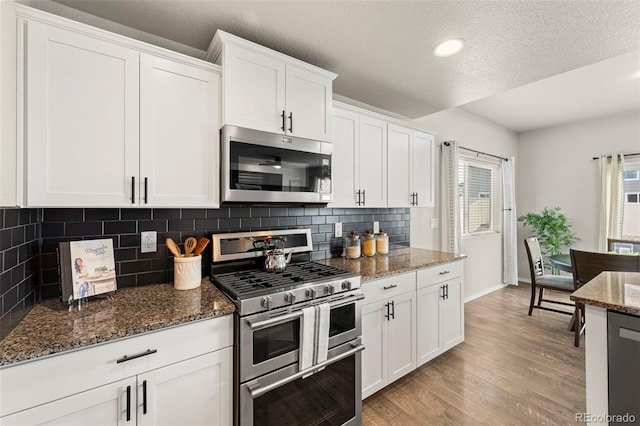 9869 Meridian Hills Trl, Peyton, CO 80831 - kitchen with stainless steel appliances, light wood finished floors, decorative backsplash, white cabinetry, and a textured ceiling