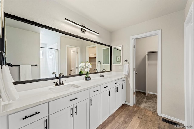 9869 Meridian Hills Trl, Peyton, CO 80831 - bathroom featuring a walk in closet, double vanity, wood finished floors, and curtained shower