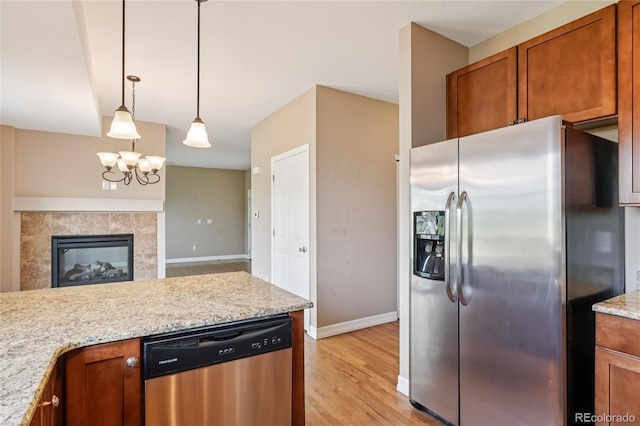 12921 Grant Cir Unit B, Thornton, CO 80241 - kitchen featuring stainless steel appliances, brown cabinets, light wood-type flooring, hanging light fixtures, and light stone counters