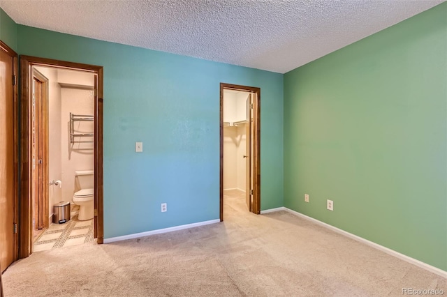 unfurnished bedroom featuring connected bathroom, light carpet, a textured ceiling, and a walk in closet