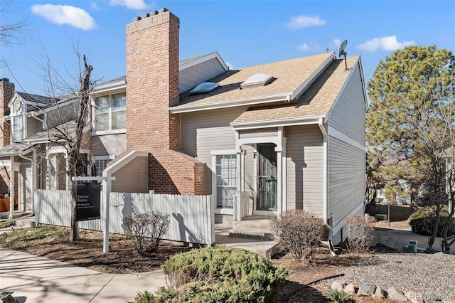 view of front of house featuring a shingled roof, a chimney, and fence