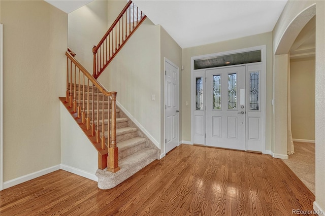 foyer with stairs, arched walkways, baseboards, and wood finished floors