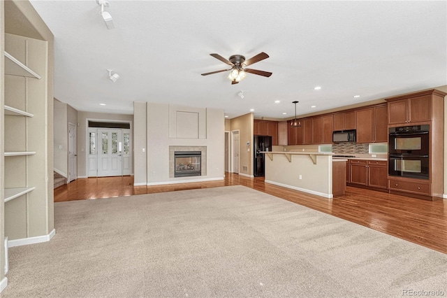 kitchen with brown cabinets, light wood-style flooring, open floor plan, black appliances, and a kitchen breakfast bar