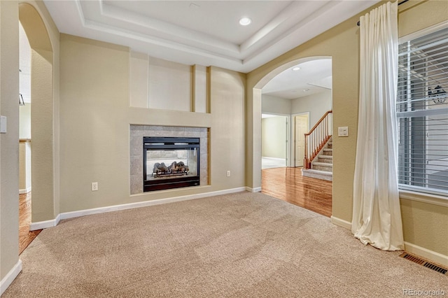 unfurnished living room featuring arched walkways, carpet floors, visible vents, baseboards, and a tiled fireplace