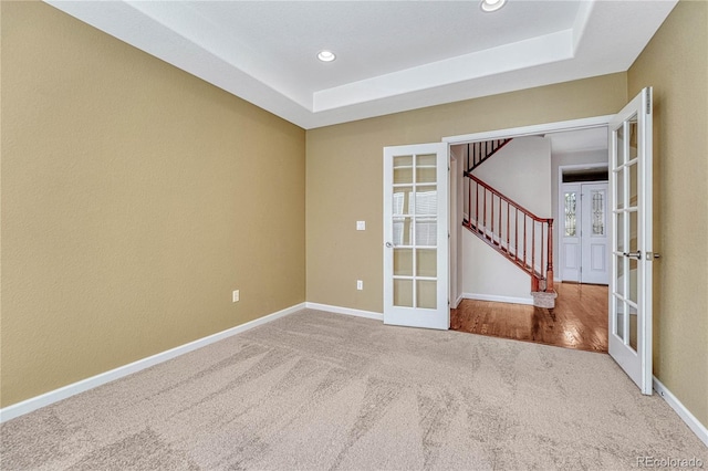 carpeted spare room featuring baseboards, stairs, a tray ceiling, french doors, and recessed lighting