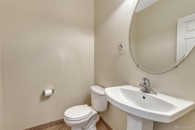 half bath featuring baseboards, a textured wall, toilet, tile patterned flooring, and a sink