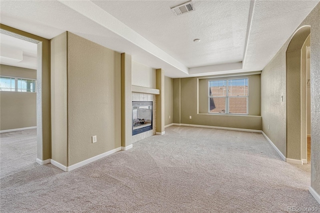 unfurnished living room featuring a textured ceiling, a textured wall, carpet, visible vents, and a tiled fireplace