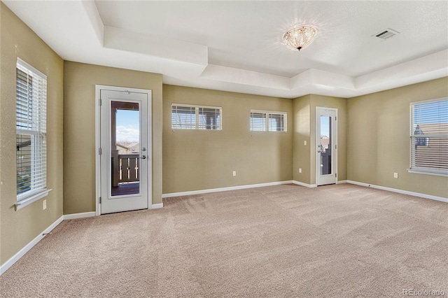 unfurnished room featuring a tray ceiling, visible vents, light carpet, and baseboards