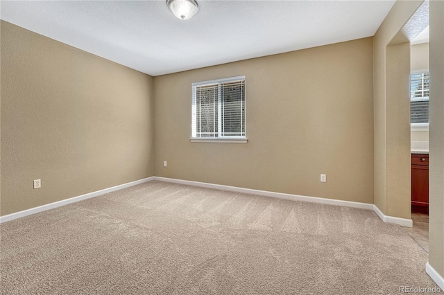 spare room with light carpet, a textured wall, and baseboards