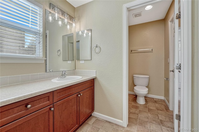 bathroom featuring toilet, vanity, visible vents, and baseboards