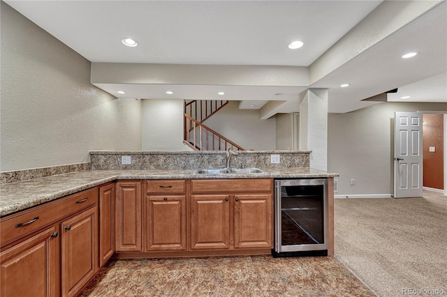 kitchen featuring brown cabinets, beverage cooler, light carpet, and a sink