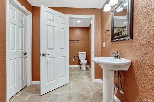 bathroom featuring toilet, tile patterned flooring, baseboards, and a textured wall