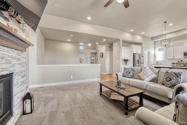 carpeted living room featuring a fireplace and ceiling fan with notable chandelier