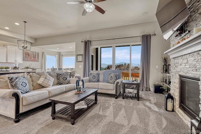 carpeted living room featuring a fireplace and ceiling fan with notable chandelier