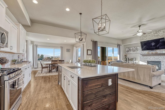 kitchen with white cabinetry, stainless steel gas range oven, a kitchen island with sink, and sink