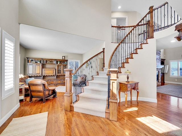 staircase featuring baseboards, a high ceiling, wood finished floors, and a fireplace