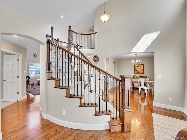 staircase featuring wood finished floors, baseboards, arched walkways, a towering ceiling, and a notable chandelier