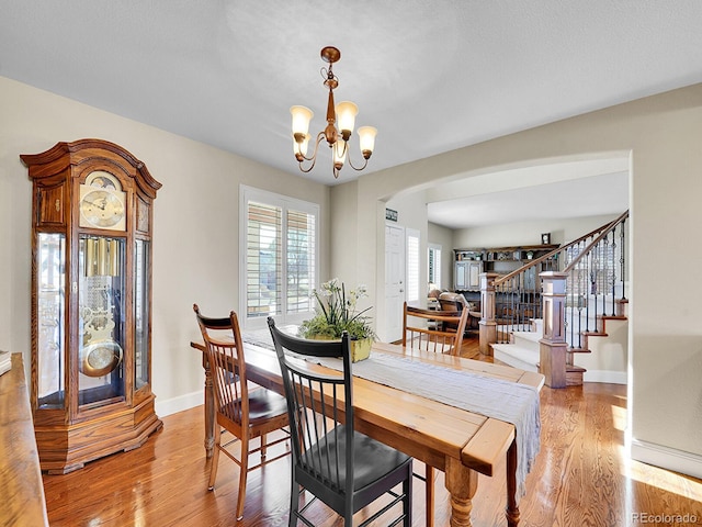 dining space featuring baseboards, light wood-type flooring, stairs, arched walkways, and a notable chandelier