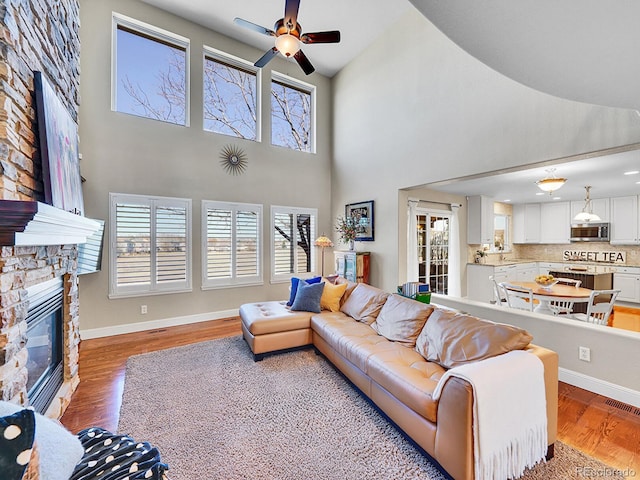 living room featuring visible vents, baseboards, light wood-type flooring, a stone fireplace, and a ceiling fan