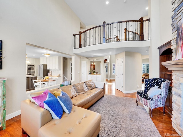 living room with light wood finished floors, baseboards, stairway, a fireplace, and a high ceiling