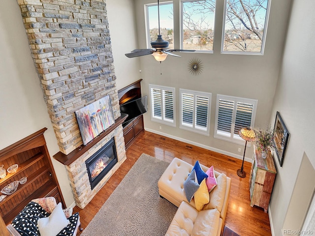 living area with a ceiling fan, wood finished floors, a high ceiling, a fireplace, and baseboards