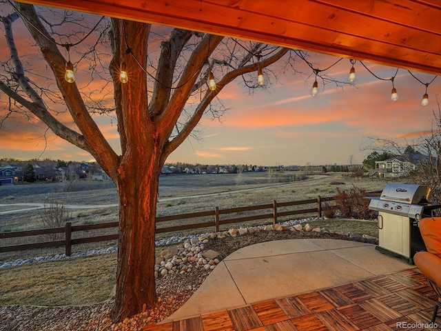 patio terrace at dusk with a rural view, area for grilling, and fence