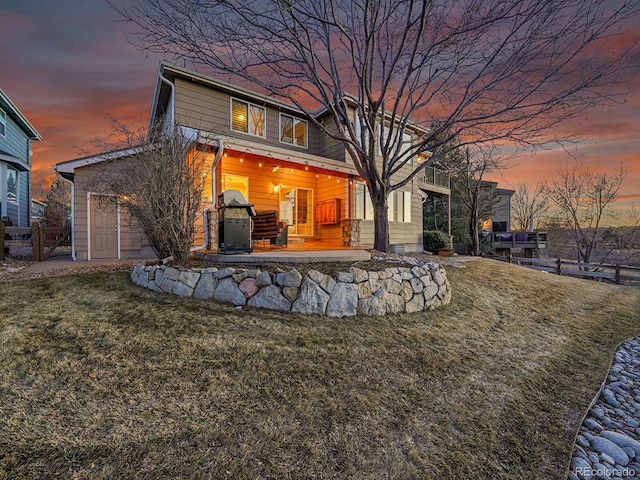 back of house at dusk featuring a yard and fence