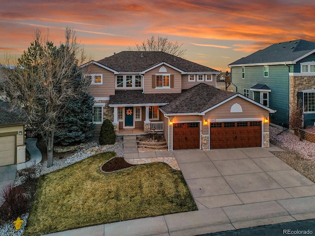 view of front of home with a front yard, covered porch, driveway, stone siding, and an attached garage