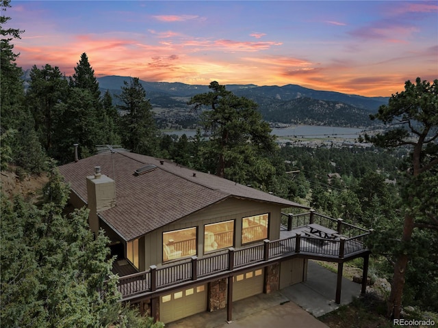 1141 Koral Ct, Estes Park, CO 80517 - rear view of house featuring a garage, roof with shingles, stone siding, a deck with mountain view, and a chimney