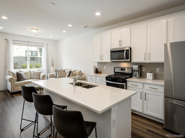 kitchen with dark hardwood / wood-style flooring, stainless steel appliances, white cabinetry, an island with sink, and sink